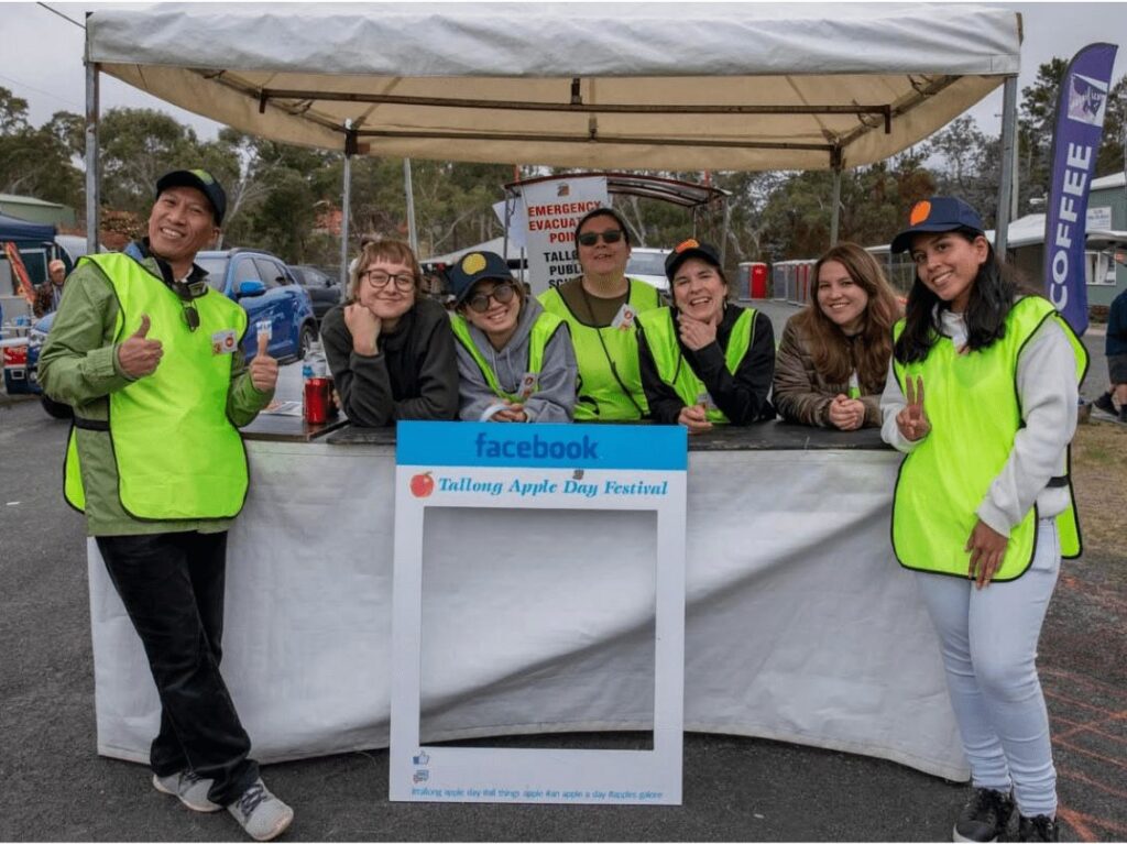 Seven volunteers, most in high-visibility vests, giving a thumbs up at a Tallong Apple Day Festival stall.